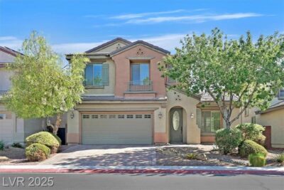 A beautiful two-story home with a warm, peach-colored exterior, green shutters, and a well-maintained front yard featuring lush trees and shrubs. The home includes a two-car garage and a charming arched front door.