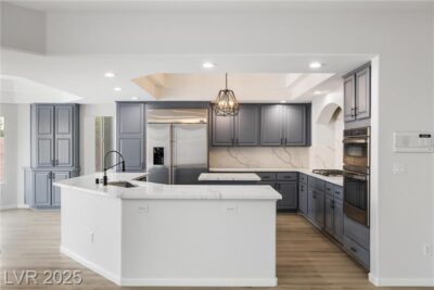 A modern kitchen with blue cabinetry, white marble countertops, stainless steel appliances, and a pendant light fixture over a spacious island. The open layout is complemented by wood flooring and recessed lighting.