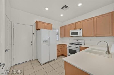 A bright and clean kitchen with light wood cabinetry, white countertops, and white appliances, including a refrigerator, gas stove, microwave, and dishwasher. The space features recessed lighting, tiled flooring, and a neutral color palette.