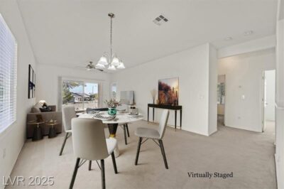 A virtually staged dining and living area with neutral tones, featuring a modern dining table with four upholstered chairs, a sleek console table with decorative artwork, and a cozy seating area near a large sliding glass door leading to an outdoor view. A ceiling fan and elegant chandelier add warmth to the space.