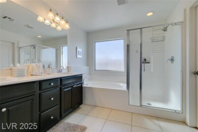 Modern bathroom with a dark vanity, double sink, mirror, a bathtub, and a glass-enclosed shower. Tiled floor and a frosted window are present.