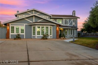 A stunning two-story home with a gray and white exterior, large windows, and a spacious driveway, set against a vibrant sunset sky.