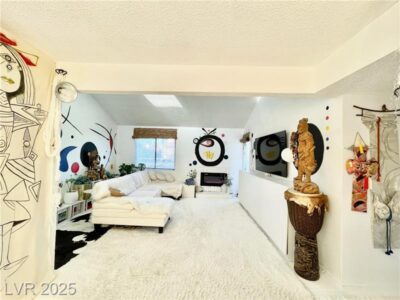 Modern living room with white shag carpet, a white sectional sofa, and artistic wall murals featuring abstract and surreal designs. Includes cultural statues and decor, and a mounted TV opposite a large window.