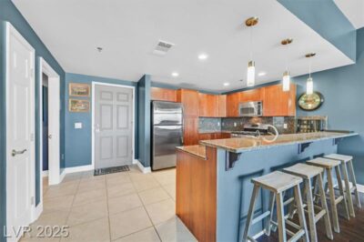 Modern kitchen with granite countertops, pendant lighting, stainless steel appliances, and a breakfast bar with four stools in a blue-painted open-concept space.