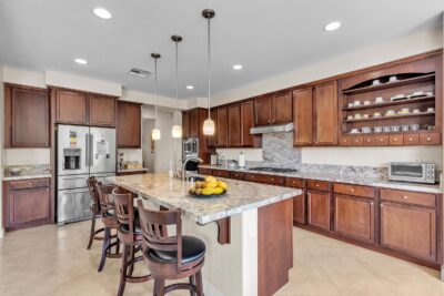 Spacious kitchen with granite countertops, rich wood cabinetry, stainless steel appliances, and a large center island with pendant lighting and bar seating.