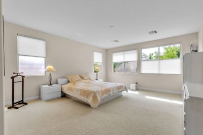 Spacious bedroom with neutral carpeting, large windows, and natural light, featuring a low-profile bed and modern furnishings.