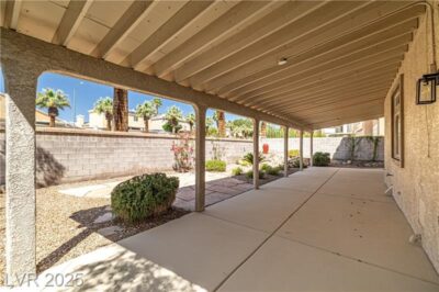 Covered backyard patio with concrete flooring, desert landscaping, and block privacy wall on a sunny day.