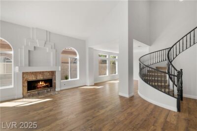Open living room with wood floors, large windows, modern fireplace, and curved staircase with black railing.