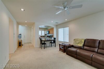 Open-concept living room with neutral carpeting, recessed lighting, a ceiling fan, and a view into the kitchen with a breakfast bar and wood cabinetry.