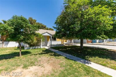 Front view of a charming single-story mid-century home with yellow and white exterior, mature trees, and a shaded front yard in Westleigh, Las Vegas.